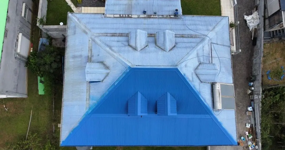 Vue aérienne d'une toiture en cours de traitement, un versant repeint en bleu, l'autre encore patiné